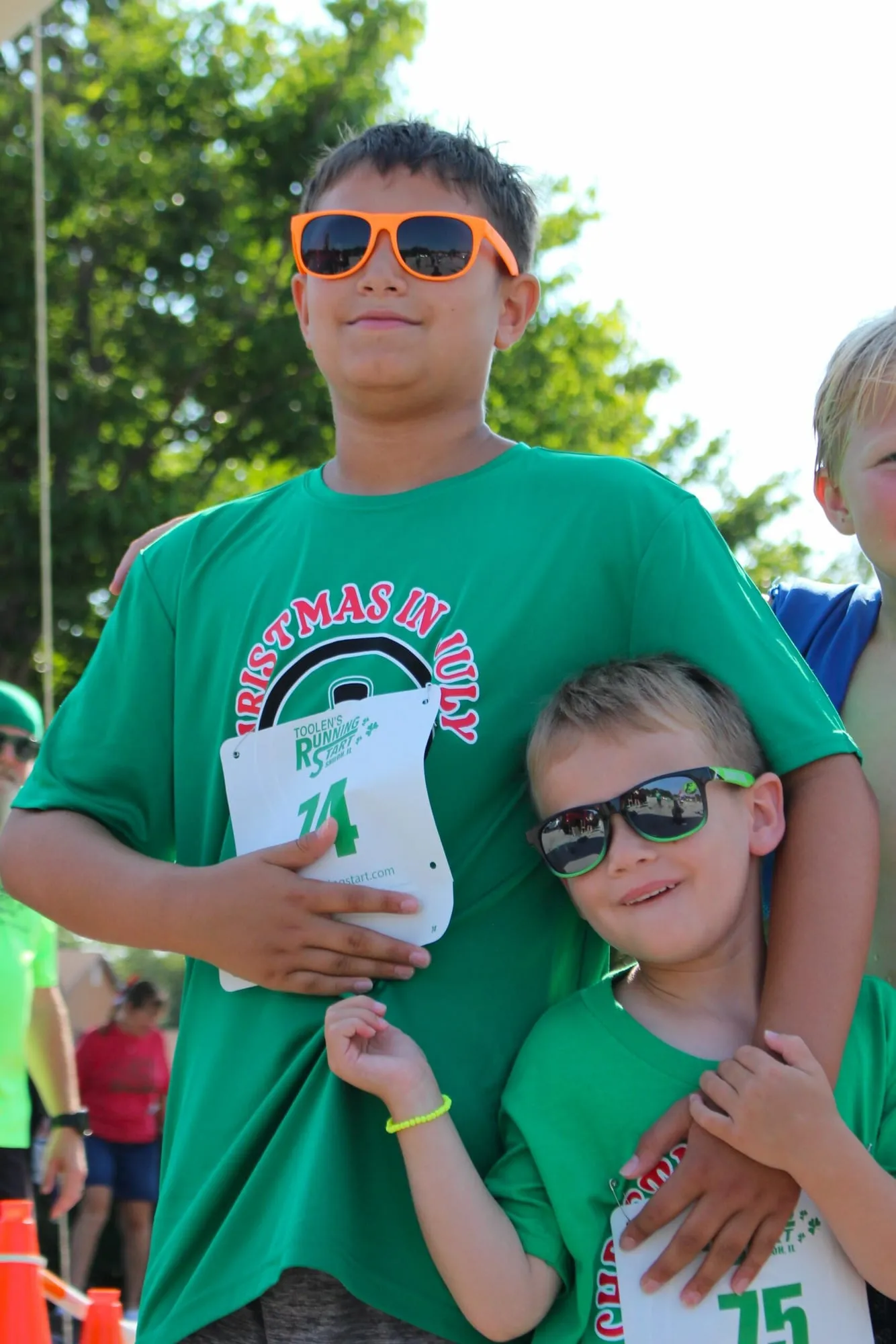 An older boy wearing bib 74 with his arm around a younger boy in sunglasses.