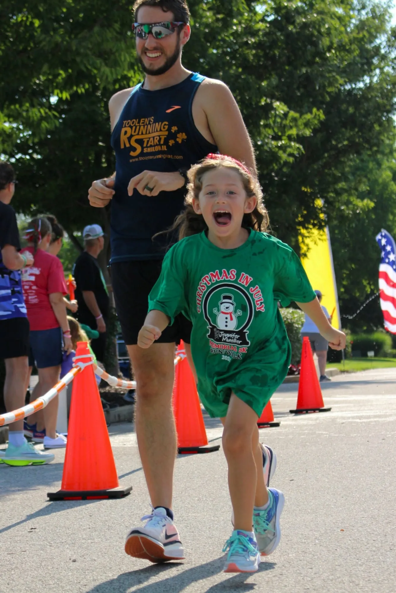A girl in a green race shirt cheering with her mouth wide open.
