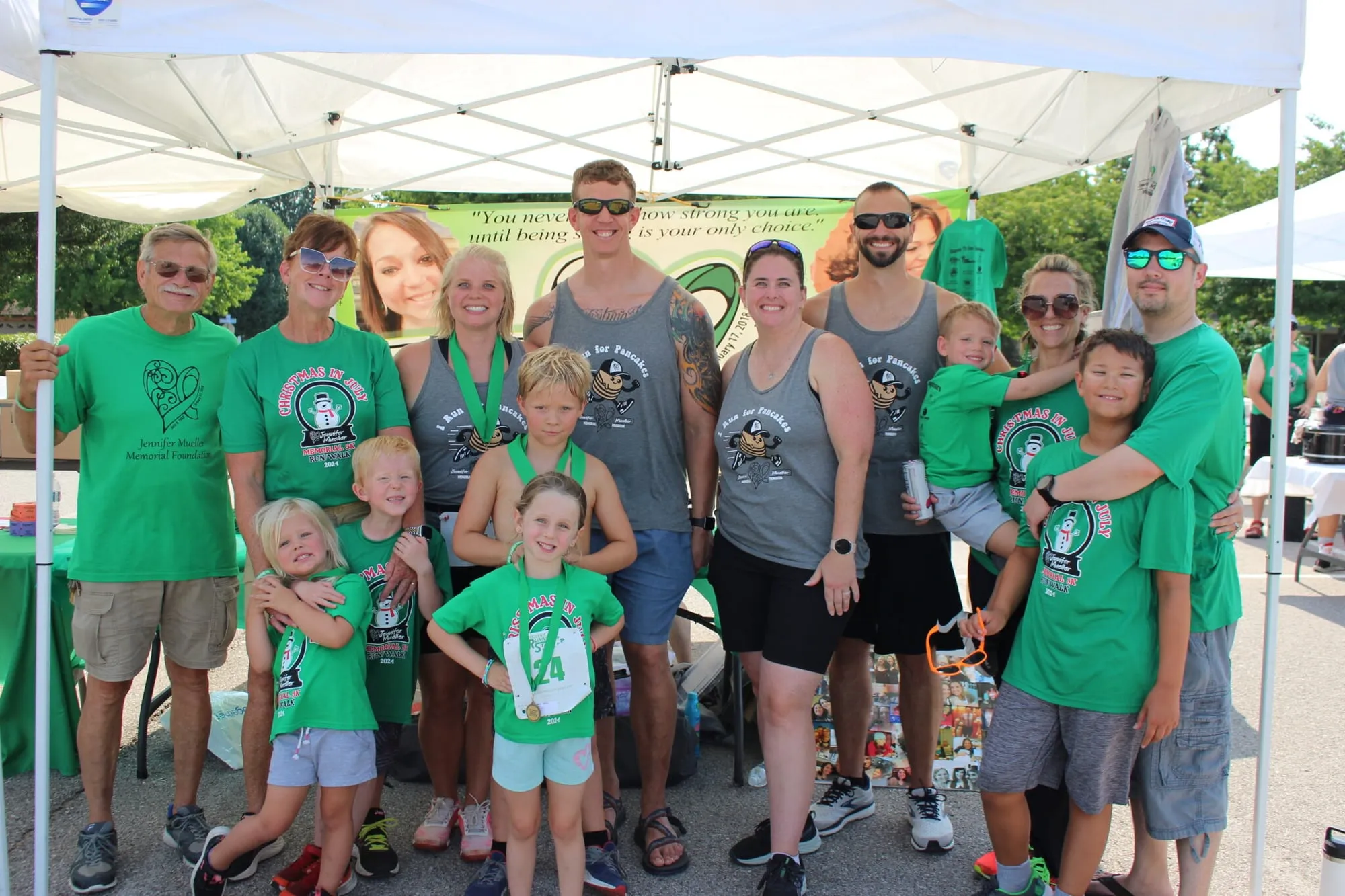 A large group of volunteers and family members posing together under the tent after the race.