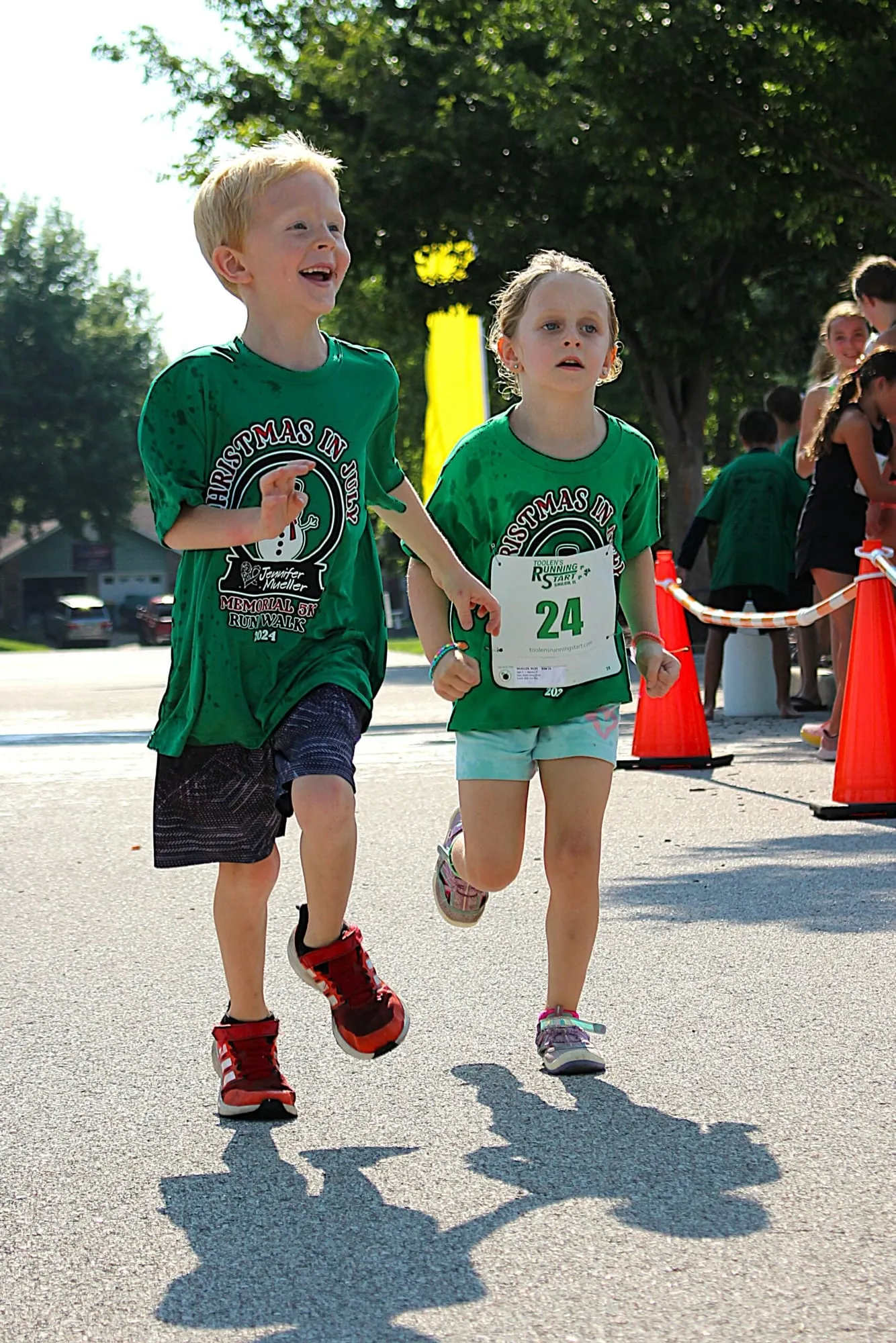 A child in a green race shirt with bib 24 running hard toward the camera.