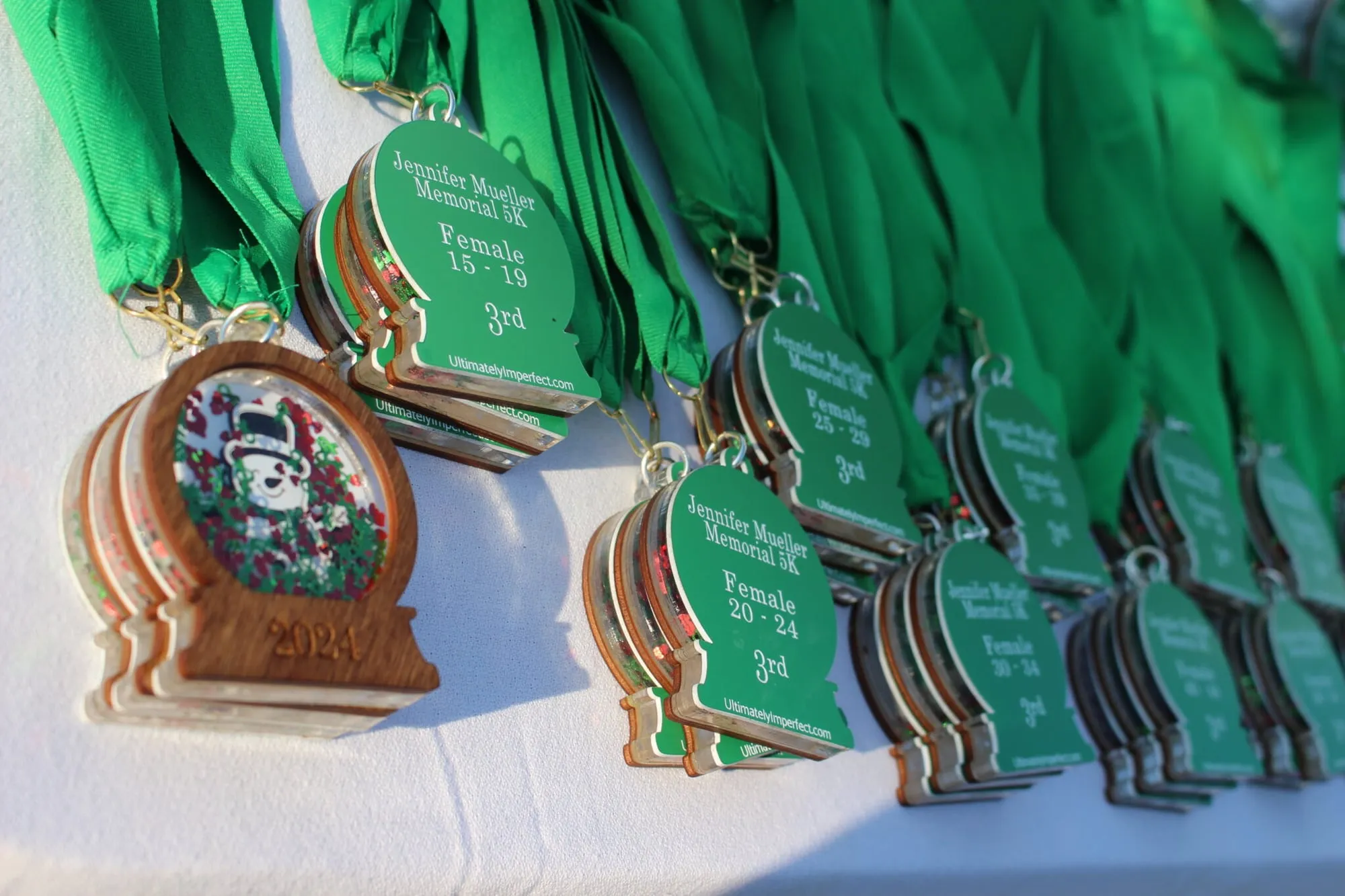 A table laid out with rows of green finisher medals and wooden ornament awards.