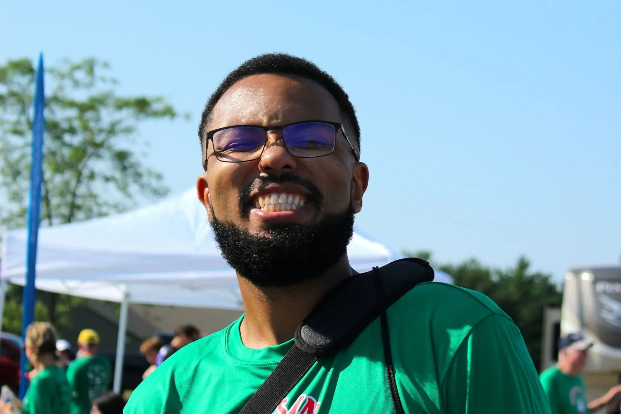 A smiling man in a green race shirt and sunglasses at the finish area.