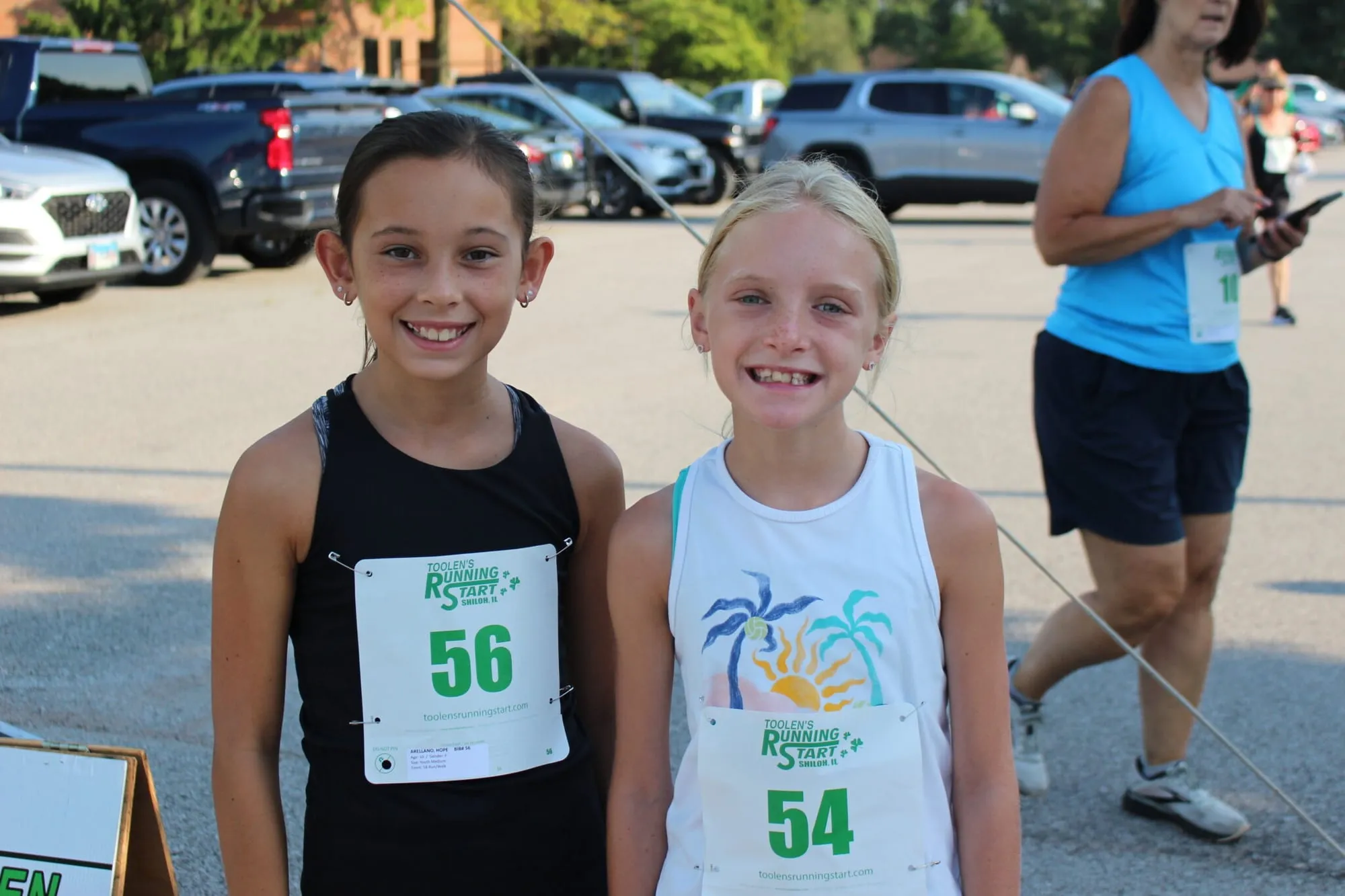 Two young girls wearing race bibs 56 and 54 standing together before the start.