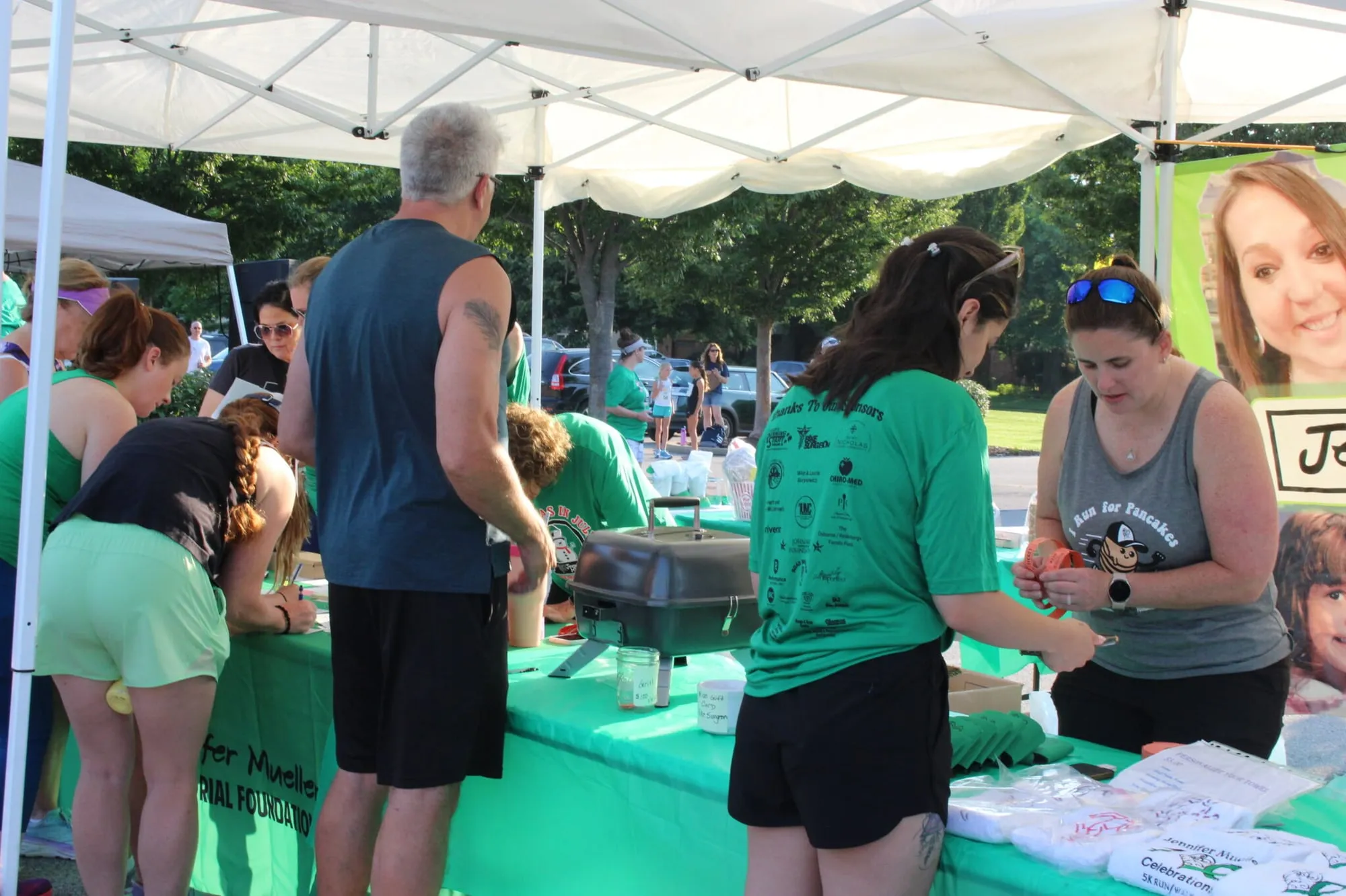 Volunteers handing out food and drinks to runners under a white tent.